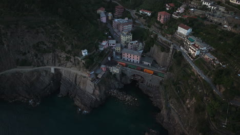 Riomaggiore,-cinque-terre,-italy-at-dusk-with-a-train-entering-a-tunnel,-aerial-view