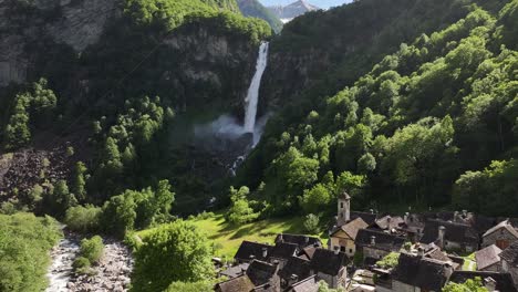 Aerial-drone-view-flying-over-Vallemaggia-in-Switzerland-with-an-impressive-waterfall-crashing-against-the-rocks