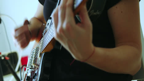 Beautiful-closed-slow-motion-shot-of-a-young-woman's-hands-and-fingers-playing-an-electric-guitar-in-a-recording-studio-with-dim-entry-light-through-the-balcony