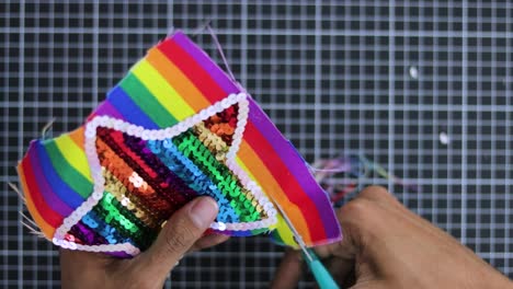 Close-up-of-hands-crafting-rainbow-themed-sequined-star-decoration-on-checkered-surface