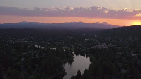 Sunset-in-Bend-Oregon-over-a-river-with-a-wooden-bridge-with-the-Cascade-mountains-and-pink-clouds-in-background