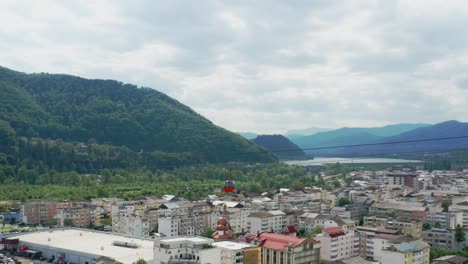 Malerische-Luftaufnahme-Einer-Kleinen-Stadt-Zwischen-üppigen-Grünen-Hügeln-Und-Einem-Ruhigen-Fluss