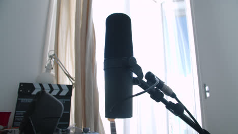 Beautiful-slow-motion-shot-of-a-famous-Shure-brand-microphone-ready-to-use-for-a-podcast-in-a-home-studio-with-dim-light-coming-in-through-the-balcony