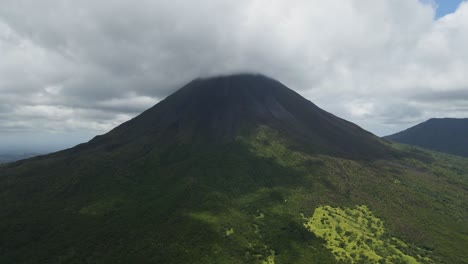 shot-from-a-drone-of-a-massive-volcano-in-the-middle-of-the-Costa-Rican-nature,-which-has-a-peak-hidden-in-the-clouds