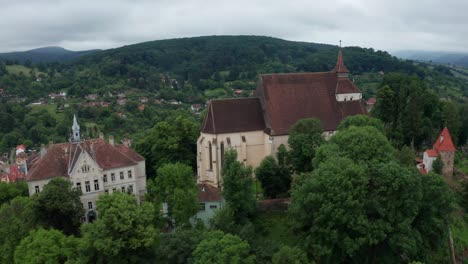 A-castle-surrounded-by-lush-greenery-and-rolling-hills-under-a-cloudy-sky,-aerial-view