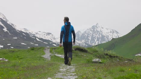 Man-hikes-through-green-meadow-with-wildflowers-in-picturesque-French-mountains