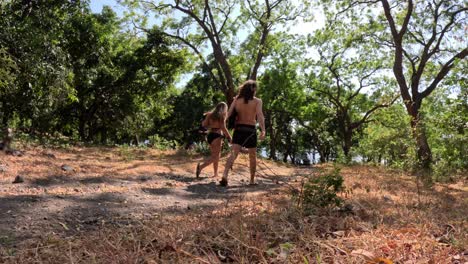 Couple-bring-fins-with-swimsuit-walk-away-on-path-at-a-lush-tropical