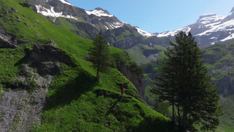 Man-Standing-On-Cliff-Overlooking-Oeschinen-Lake-In-Bernese-Oberland,-Switzerland---Aerial-Drone-Shot