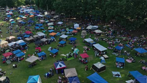 Aerial-flyover-open-air-festival-in-usa-with-crowd-of-fans-hiding-under-tent