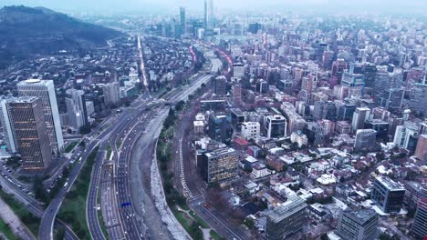 La-Vista-Aérea-Del-Dron-Permite-Descubrir-Con-Zoom-Los-Edificios-De-La-Ciudad-De-Santiago-De-Chile,-Las-Rutas,-Las-Carreteras-Y-Las-Montañas-Nevadas-De-Los-Andes-En-Una-Nublada-Mañana-De-Invierno