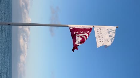 Spanish-Qualitur-and-Iso-14001-flags-for-beach-condition-quality-award-waving-in-La-Renega-Beach,-Oropesa-del-Mar,-Spain