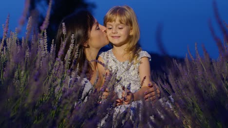 Mother-and-girl-daughter-kid-kissing,-laughing-in-aromatic-flowers-lavender-field-garden-at-night