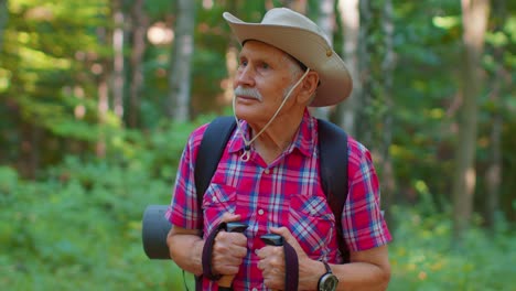 Senior-old-Caucasian-tourist-hiker-grandfather-training-Nordic-walking-with-trekking-poles-in-forest