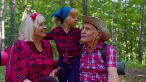 Grandmother-grandfather-and-child-kid-girl-family-hikers-tourists-sitting-in-wood,-hugging,-kissing