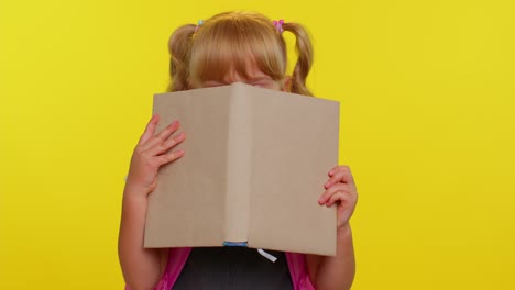 Funny-kid-primary-school-girl-with-ponytails-wearing-uniform-peeping-while-hiding-behind-a-book