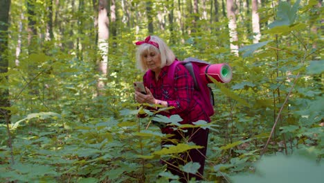 Retired-senior-elderly-grandmother-adventurer-exploring-forest-trees,-plants-with-mobile-cell-phone