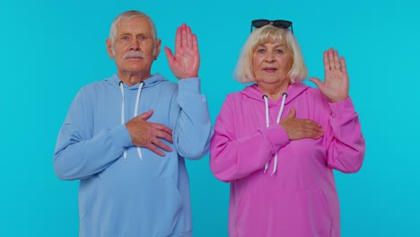 Sincere-responsible-senior-couple-man-woman-grandparents-raising-hands-to-take-oath,-tell-truth