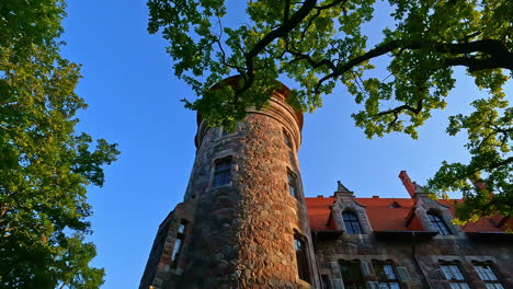 Low-angle-shot-of-famous-Cesvaine-Palace-in-Latvia-with-tree-leaves-in-foreground