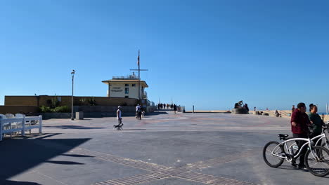 Toma-En-Cámara-Lenta-De-Lugareños-Con-Sus-Bicicletas-Y-Su-Perro-Mascota-Deambulando-Por-La-Playa-De-Manhattan-Durante-El-Día-En-California,-EE.-UU.