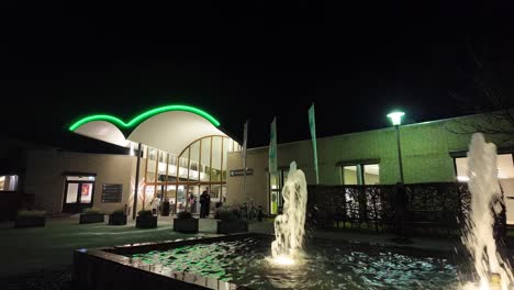 Vista-Nocturna-De-La-Entrada-Iluminada-Del-Hotel-Termal-Arcen-Con-Una-Fuente-De-Agua-Bellamente-Iluminada-En-Primer-Plano