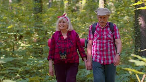 Senior-old-grandmother-grandfather-tourists-enjoying-walking,-hiking-with-backpacks-in-summer-wood