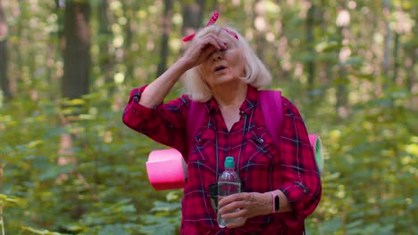 Tired-thirsty-senior-old-Caucasian-hiker-grandmother-relaxing,-drinking-water-in-forest-after-walk