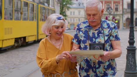 Turistas-Senior-Con-Estilo,-Hombre-Y-Mujer,-Dando-Un-Paseo-Y-Buscando-El-Camino-Usando-Un-Mapa-De-Papel-En-La-Ciudad-Vieja