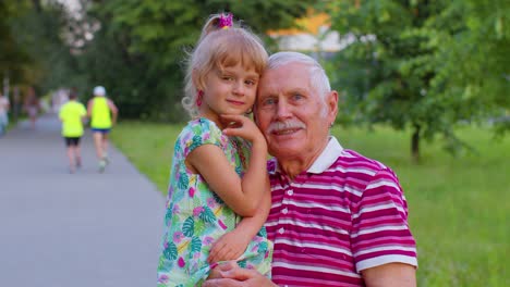 Little-granddaughter-child-embracing-kissing-with-her-grandfather-in-park,-happy-family-relationship