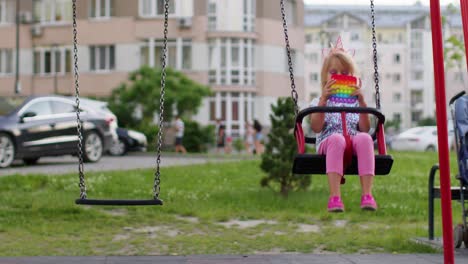 Stilvolles-Kleines-Kind-Spielt-Mit-Trendigem-Pop-it-Bubble-Squishy-Sensory-Spiel-Auf-Der-Spielplatzschaukel