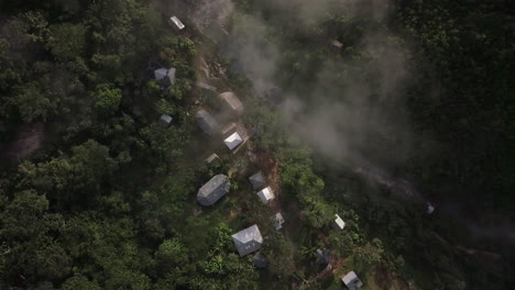 Aerial-view-of-a-small-village-in-the-dense-jungle-with-smoke-rising-from-some-buildings,-under-a-misty-sky