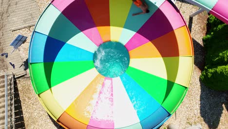 Aerial-footage-of-young-man-enjoying-a-thrilling-spin-on-a-vibrant,-colorful-water-slide-at-an-aquapark