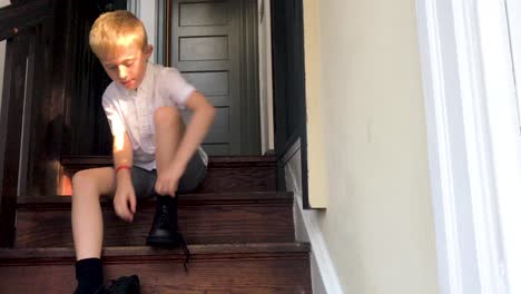 Boy-is-tying-shoes-before-school,-sitting-on-steps