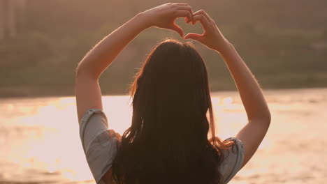 Silhouette-of-Romantic-couple's-back-in-love-doing-picnic-standing-on-the-shore-comparing-hearts,-background-for-Valentine's-day-at-sunset