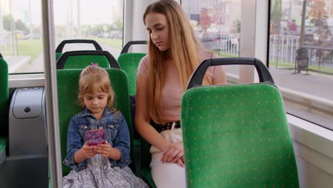 Mujer-Cansada-Y-Soñolienta-Con-Su-Hija-Yendo-A-Casa-En-Autobús-Después-De-Un-Duro-Día-De-Trabajo,-Un-Niño-Juega-En-Un-Teléfono-Inteligente