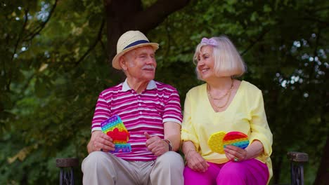 Senior-stylish-grandmother-grandfather-showing-squeezing-anti-stress-push-pop-it-popular-toy-game