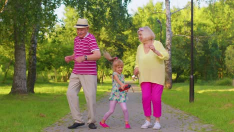 Granddaughter-together-with-senior-grandmother-grandfather-listening-to-music,-dancing-crazy-in-park