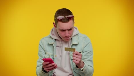 Teen-man-using-credit-bank-card-and-smartphone-while-transferring-money,-purchases-online-shopping