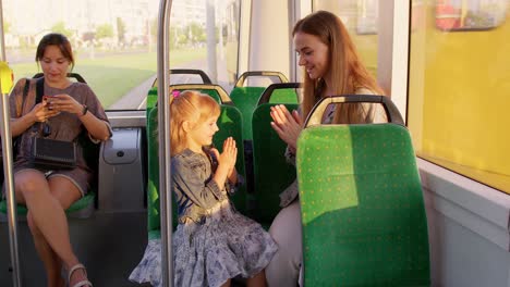 Family-rides-in-public-transport-tram,-mother-with-girl-sit-together-and-playing-game-clapping-hands