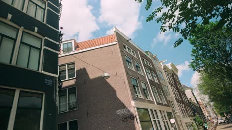 POV-movement-forward-through-Amsterdam's-historic-city-center,-showcasing-the-iconic-canal-houses-with-their-distinct-architecture-and-charm-under-a-clear-blue-sky