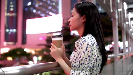 Close-up-beautiful-lonely-girl-playing-with-holding-coffee-on-the-overpass-under-high-rise-building-at-night