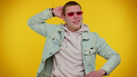 Sincere-cool-cheerful-stylish-man-in-denim-jacket-wearing-sunglasses,-charming-smile-on-yellow-wall