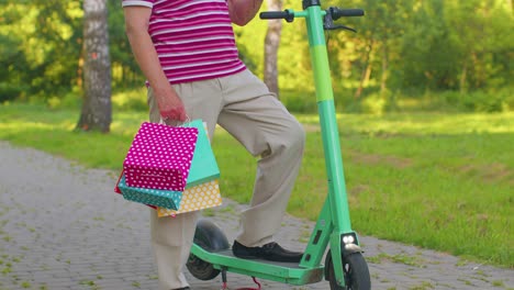 Caucasian-old-senior-grandfather-man-leaning-on-electric-scooter-after-shopping-with-colorful-bags