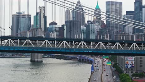 Luftaufnahme-Folgt-Autos,-Die-Die-Manhattan-Bridge-überqueren,-Mit-Der-Skyline-Von-New-York-Und-Gebäuden-Hinter-Kabeln