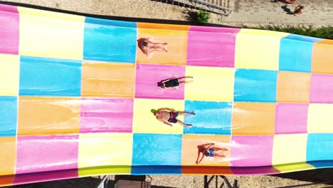 Slow-motion-aerial-clip-of-four-people-enjoying-a-vibrant,-colorful-water-slide-at-aquapark