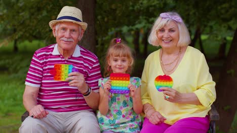 Senior-stylish-couple-grandmother-grandfather-with-granddaughter-play-anti-stress-pop-it-toy-game