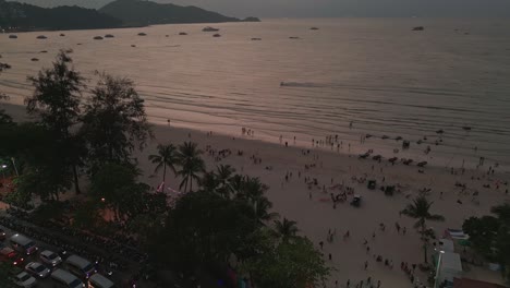 Drone-view-of-watersports-going-on-Patong-Beach-during-sunset-in-Phuket,-Thailand