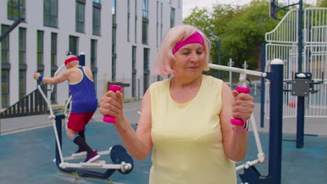 Senior-woman-grandmother-doing-active-training-weightlifting-exercising-with-dumbbell-on-playground