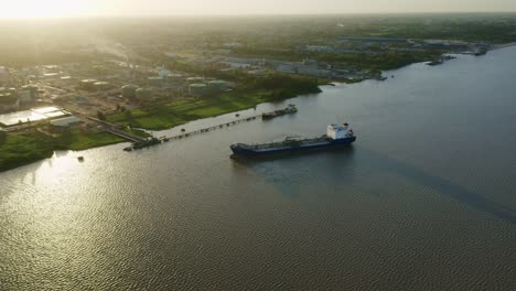 Aerial:-Oil-tanker-ship-getting-in-place-to-dock-in-Suriname-river,-sunset-in-background