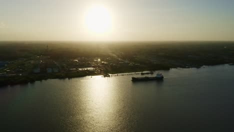 Aerial:-Oil-tanker-ship-getting-in-place-to-dock-in-Suriname-river,-sunset-in-background,-silhouette