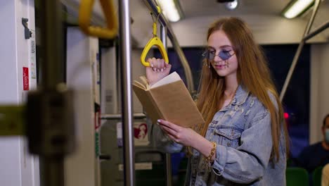 Portrait-of-attractive-young-adult-woman-stay-at-empty-subway-train-and-reading-interesting-book